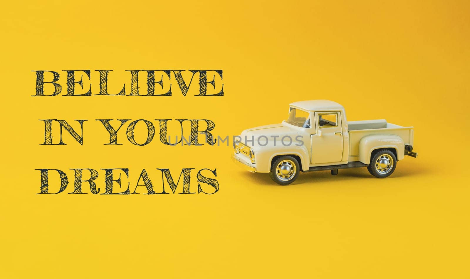 A toy truck is on a yellow background with the words believe in your dreams written below it