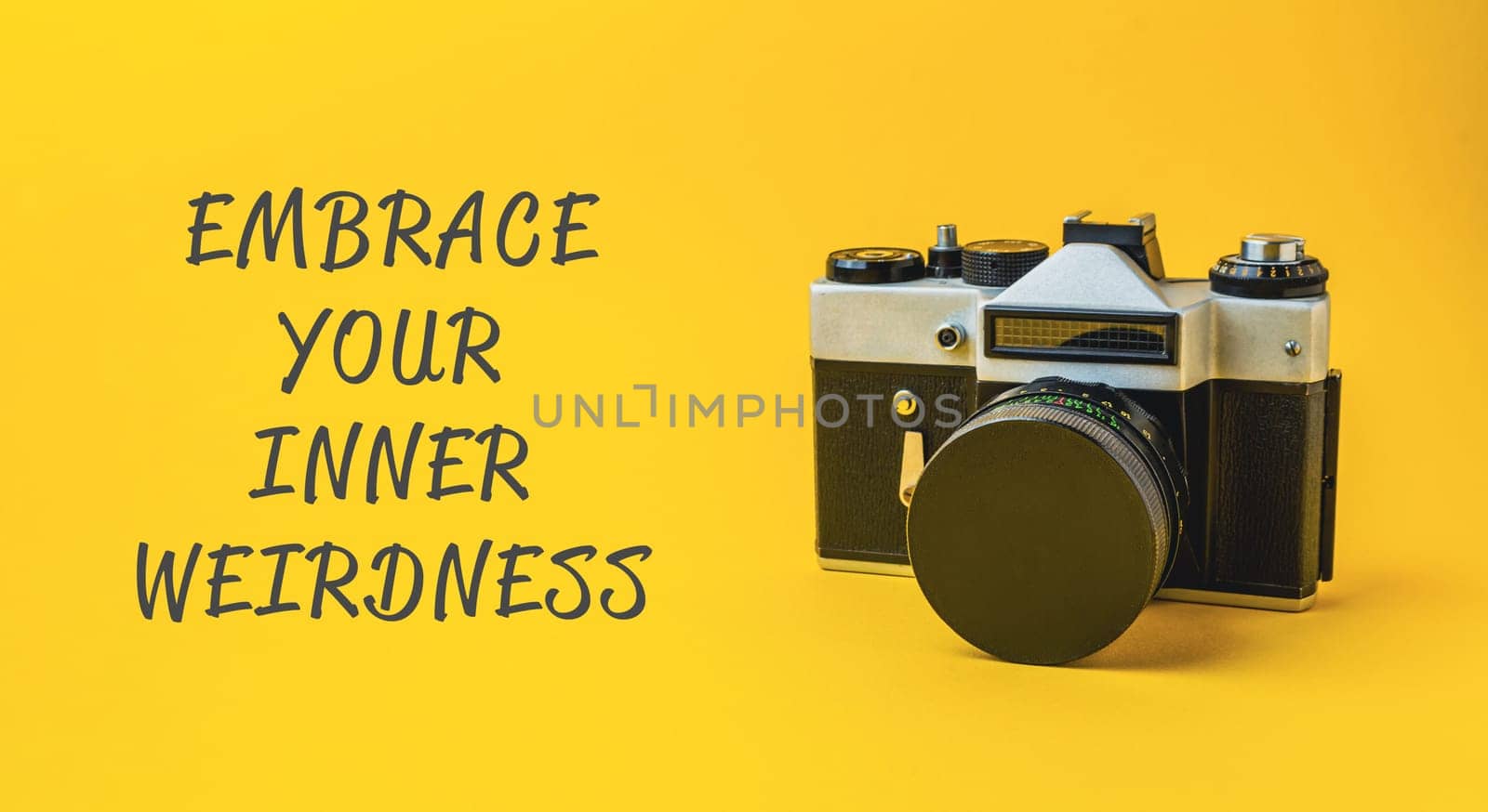 A camera with the words embrace your inner weirdness written below it. The camera is on a yellow background