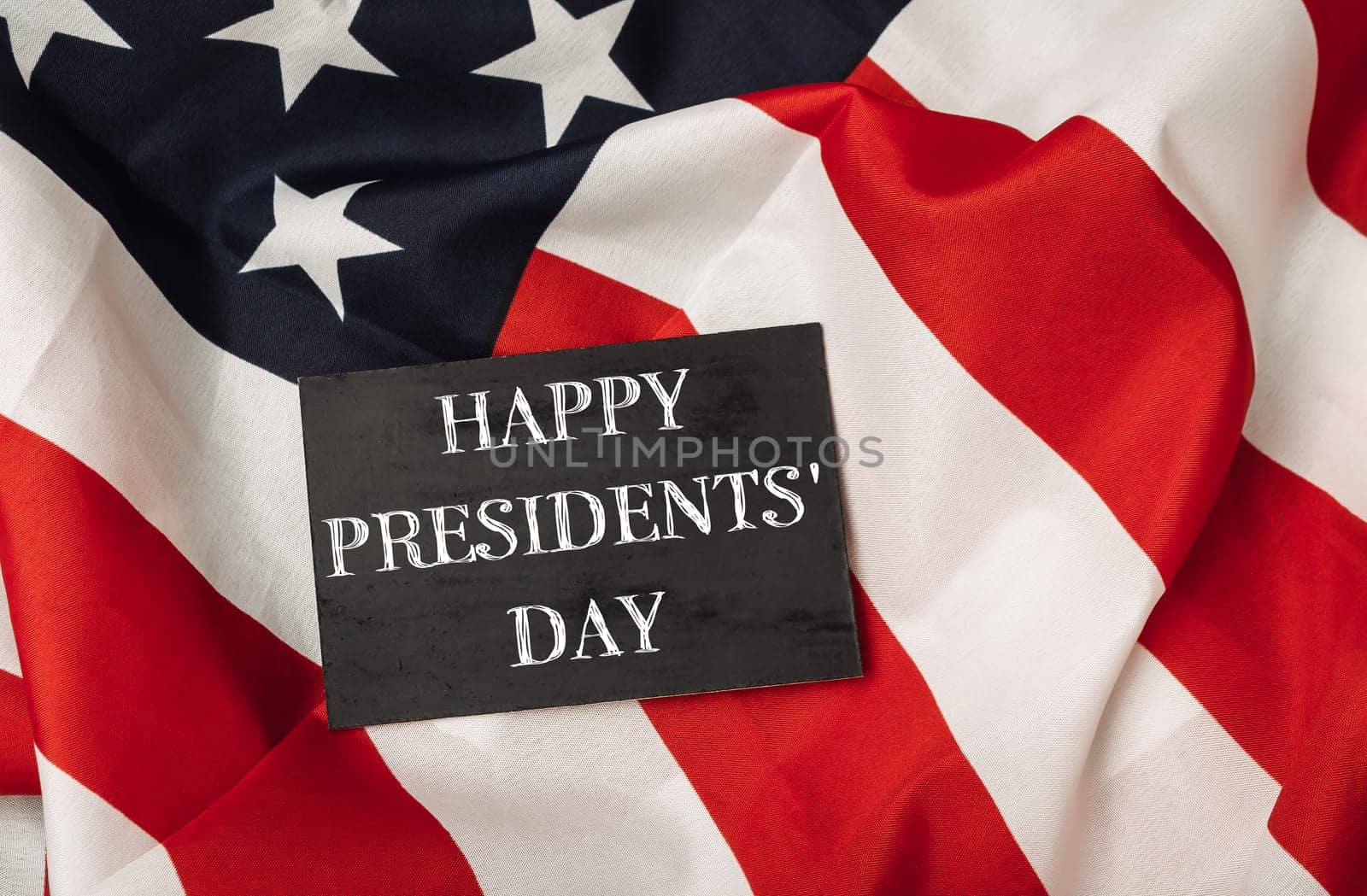 A black sign with the words Happy Presidents' Day written on it is placed on top of a red and white American flag