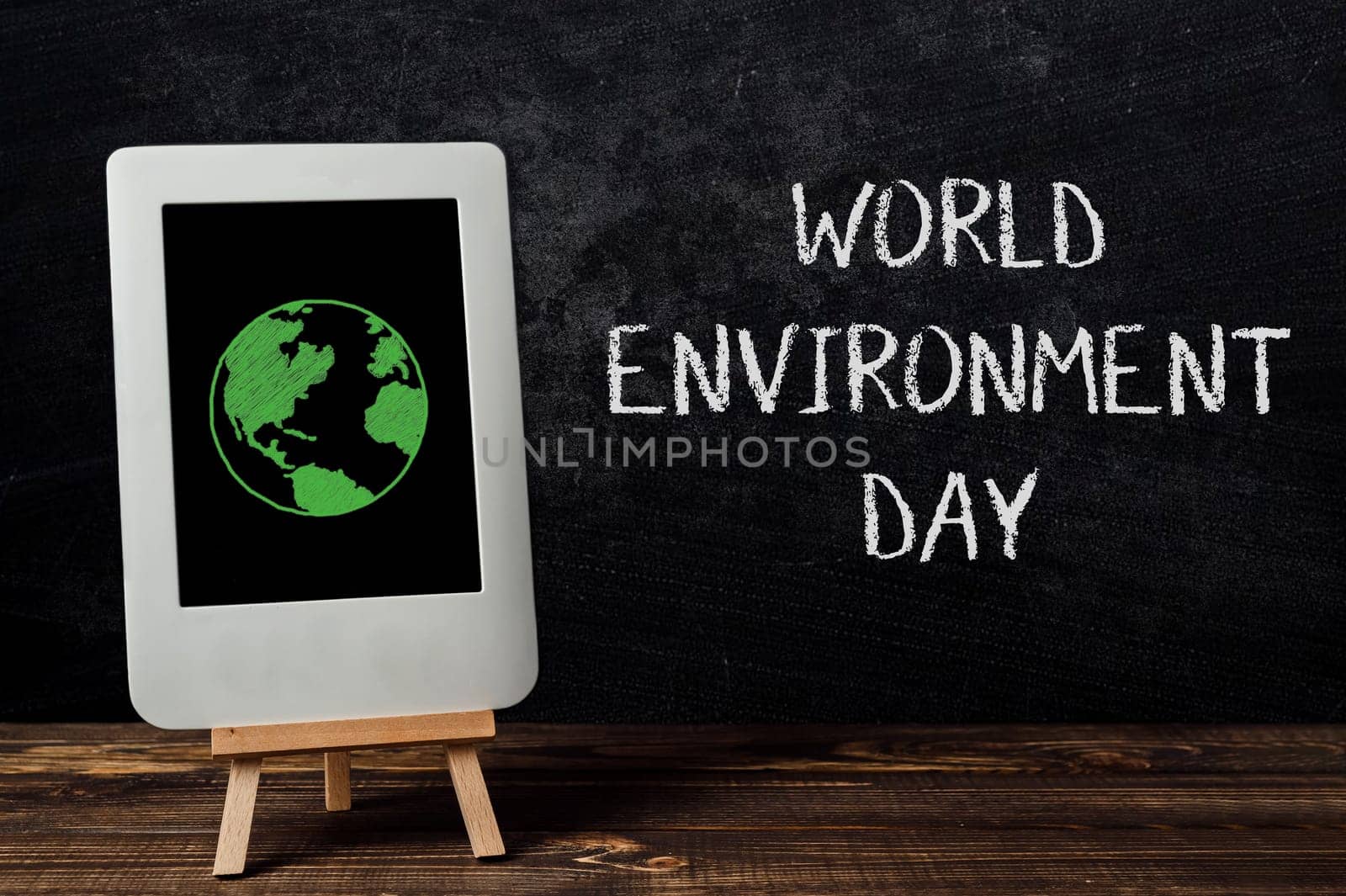 A white tablet displaying a green planet image rests on a wooden table, symbolizing environmental awareness and technology integration.