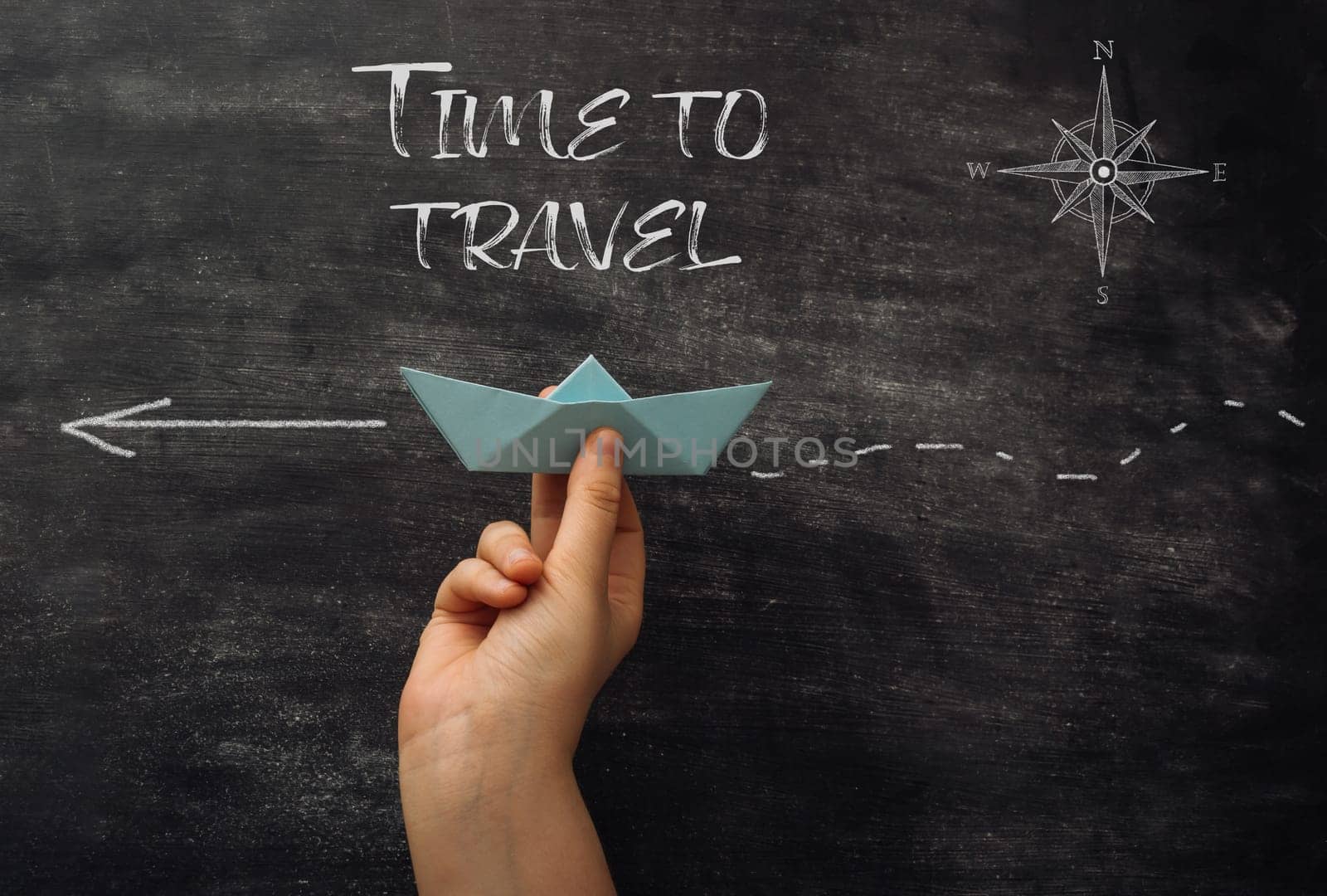 A hand holding a paper boat on a chalkboard with the words Time to Travel written above it