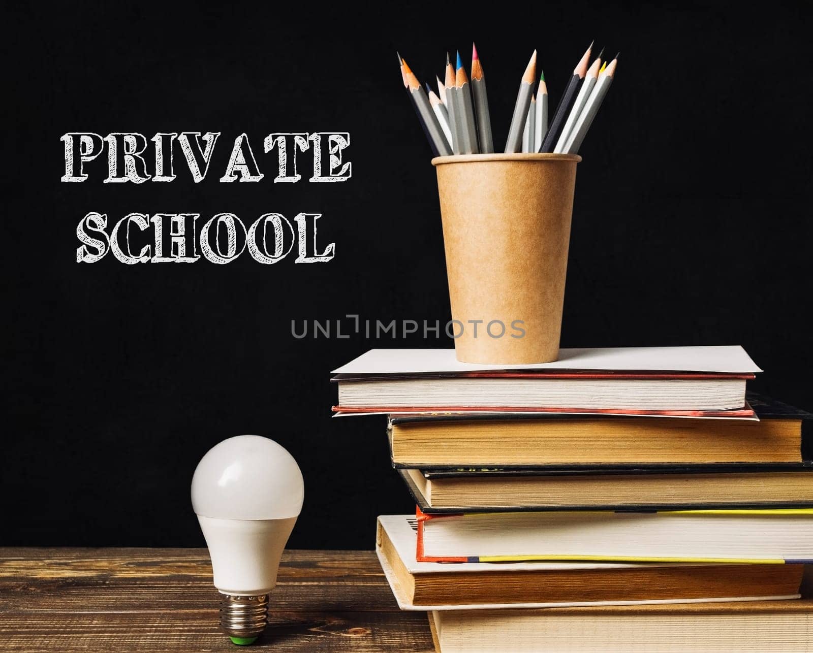 A stack of books and a light bulb on a table with the words Private School written on the table