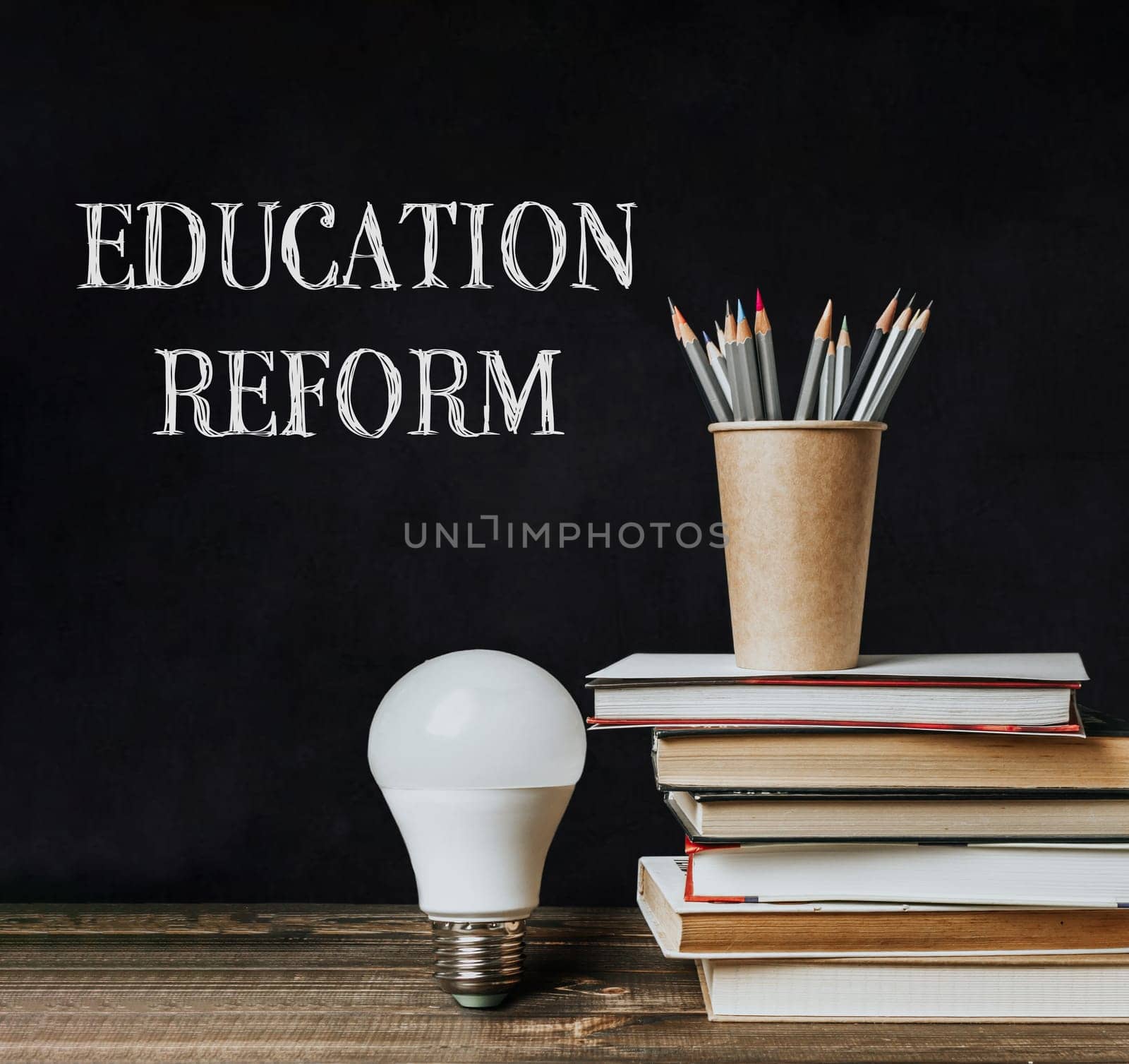 A blackboard with a white light bulb on it and a stack of books. The words Education Reform are written in black on the board