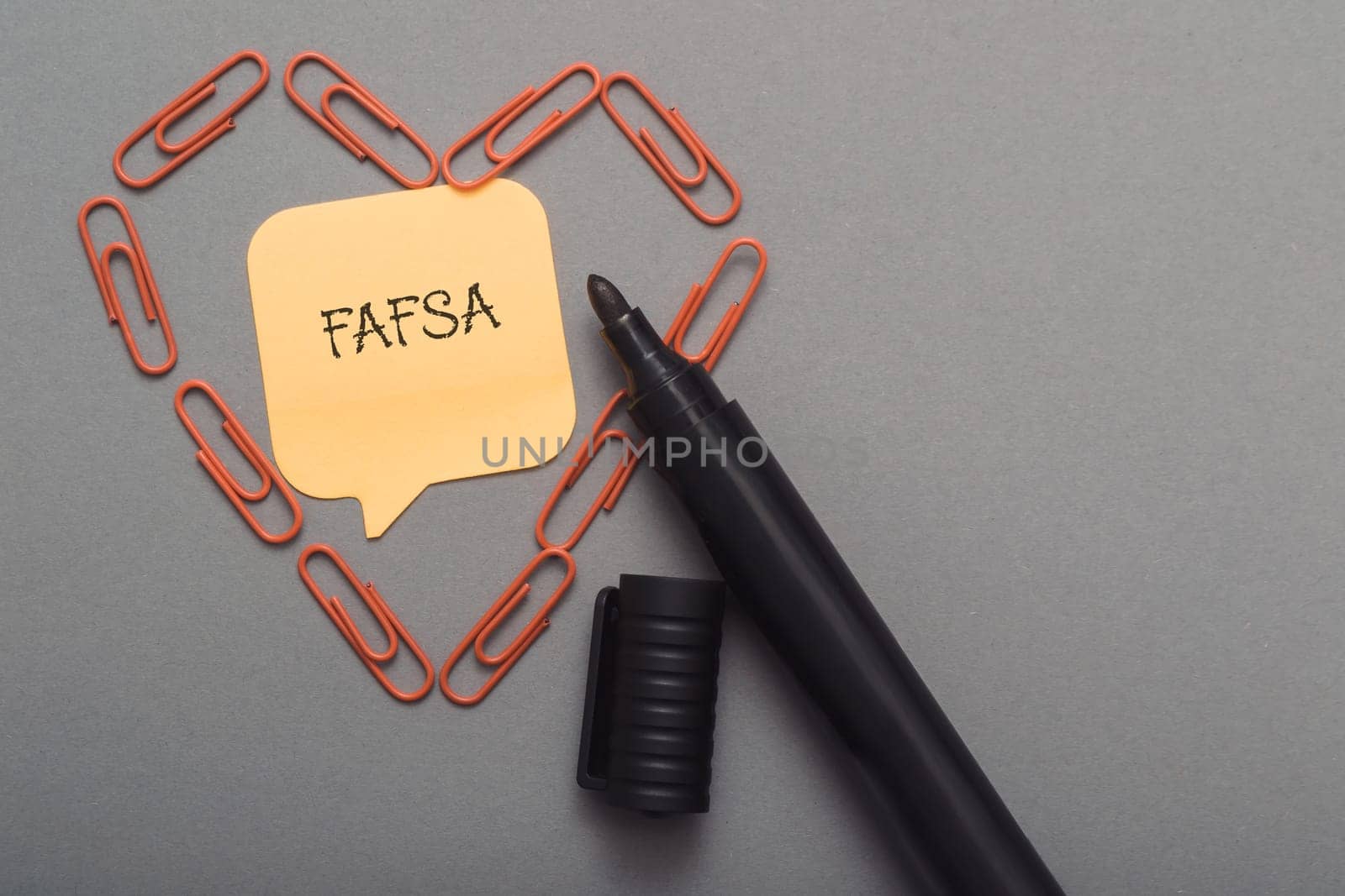 A pen with a piece of paper with the word FAFSA written on it. The pen is surrounded by paper clips, creating a heart shape