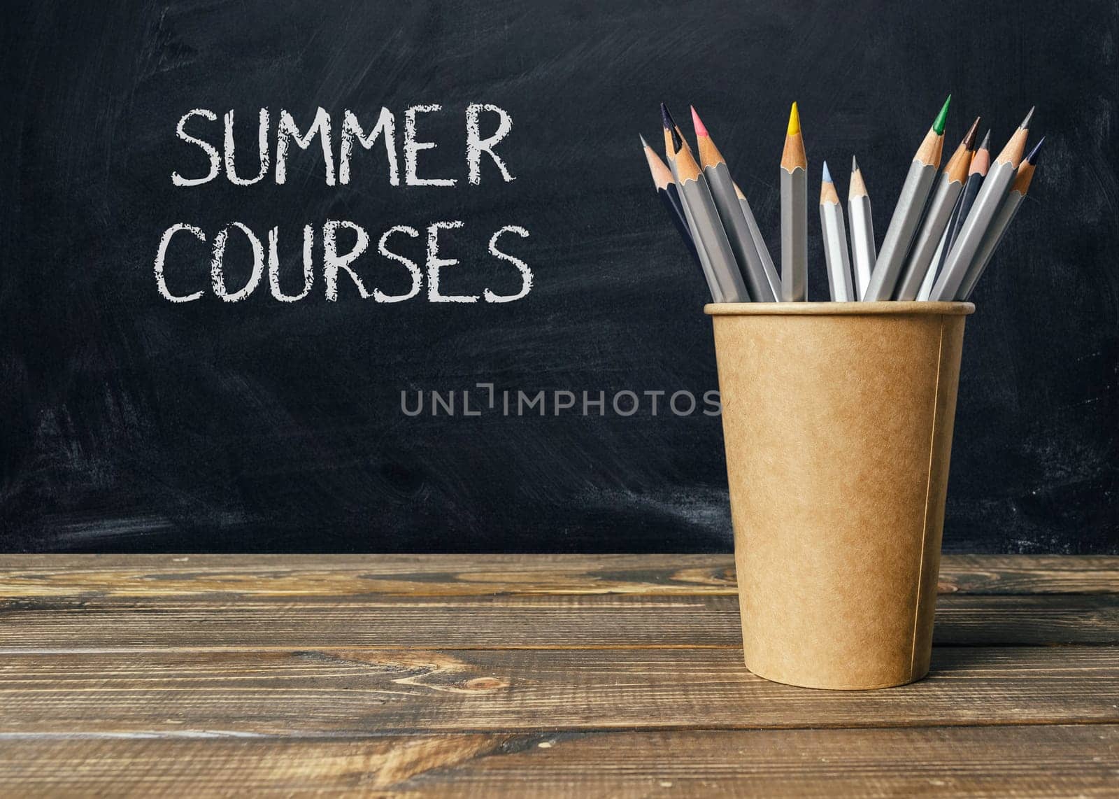 A wooden table with a cup of pencils and chalkboard with the words Summer Courses written on it