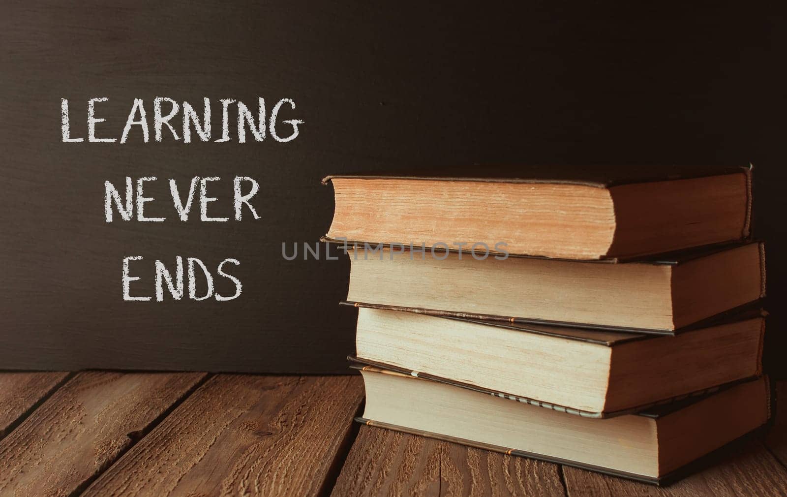 A stack of books with the words learning never ends written on a chalkboard. The books are arranged in a pyramid shape, with the top book being the largest and the bottom book being the smallest