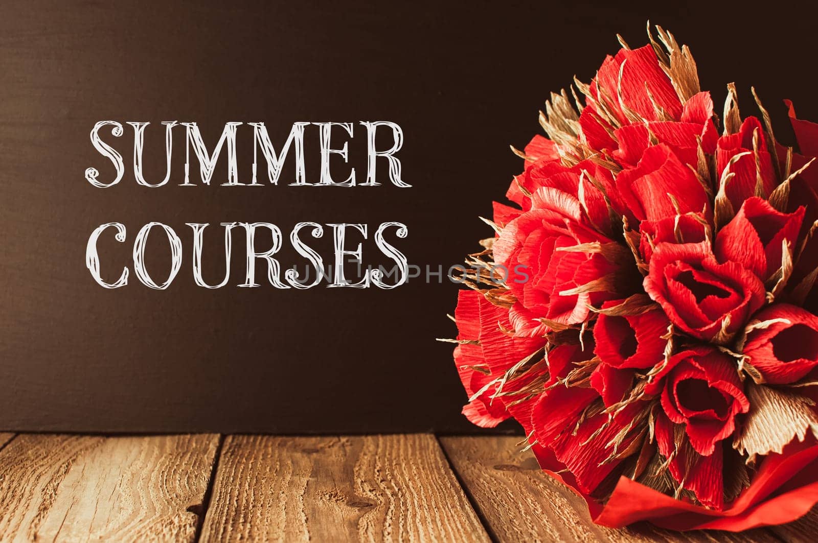 A bouquet of red flowers sits on a wooden table with the words Summer Courses written in white