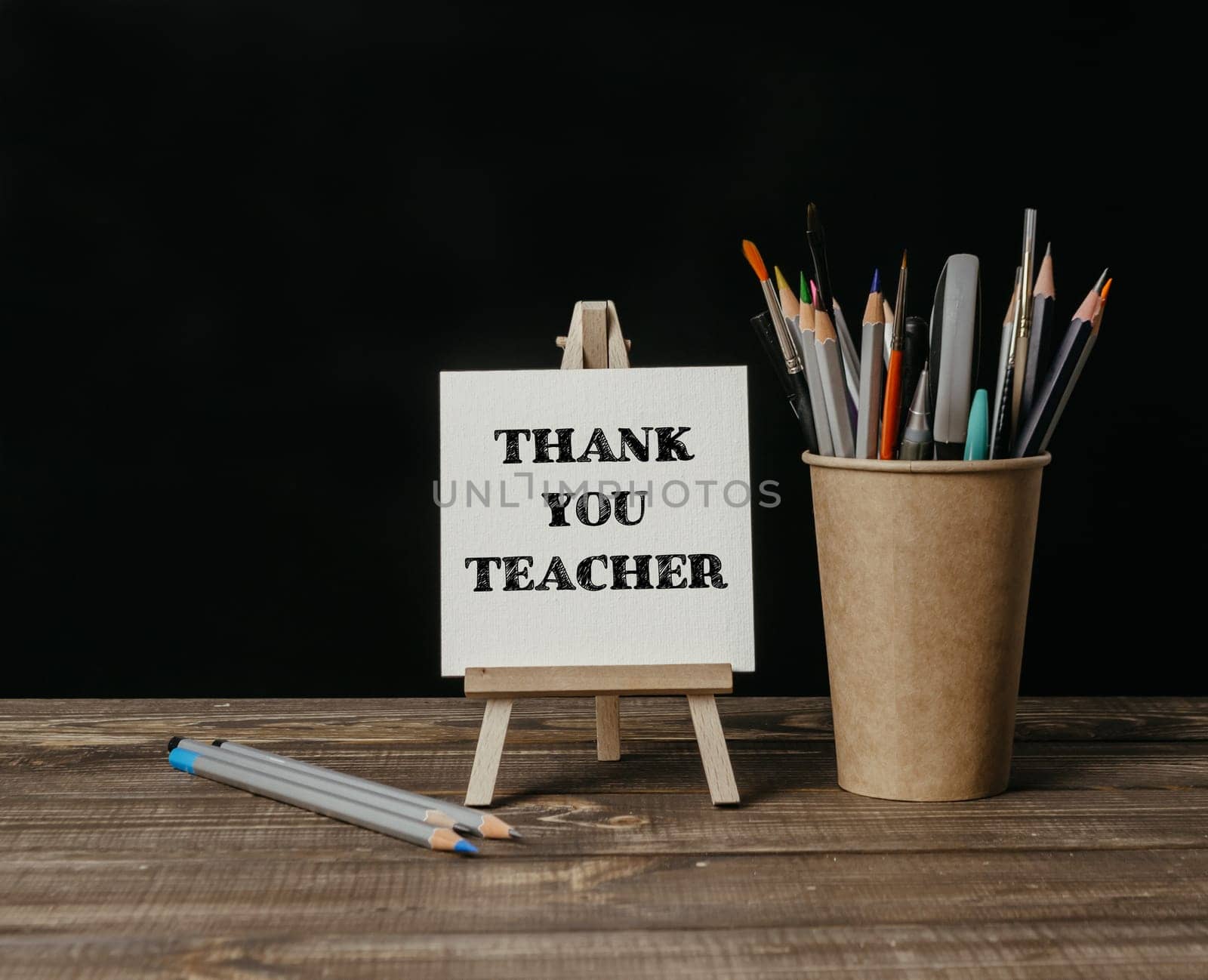A wooden desk with a sign that says Thank You Teacher and a cup of pencils