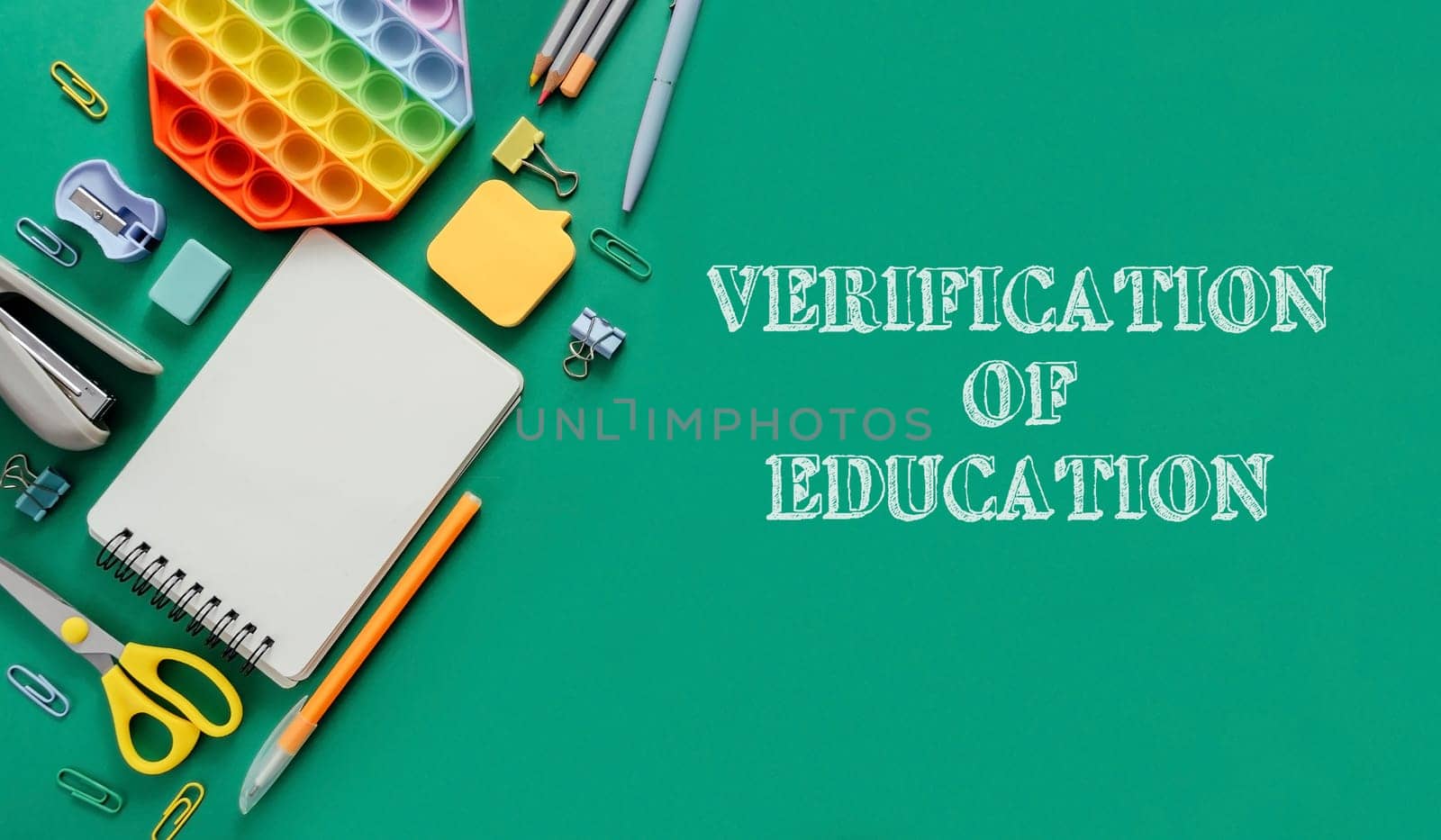 A green background with a notebook, pens, scissors, and a rubber band. The words Verification of Education are written on the background