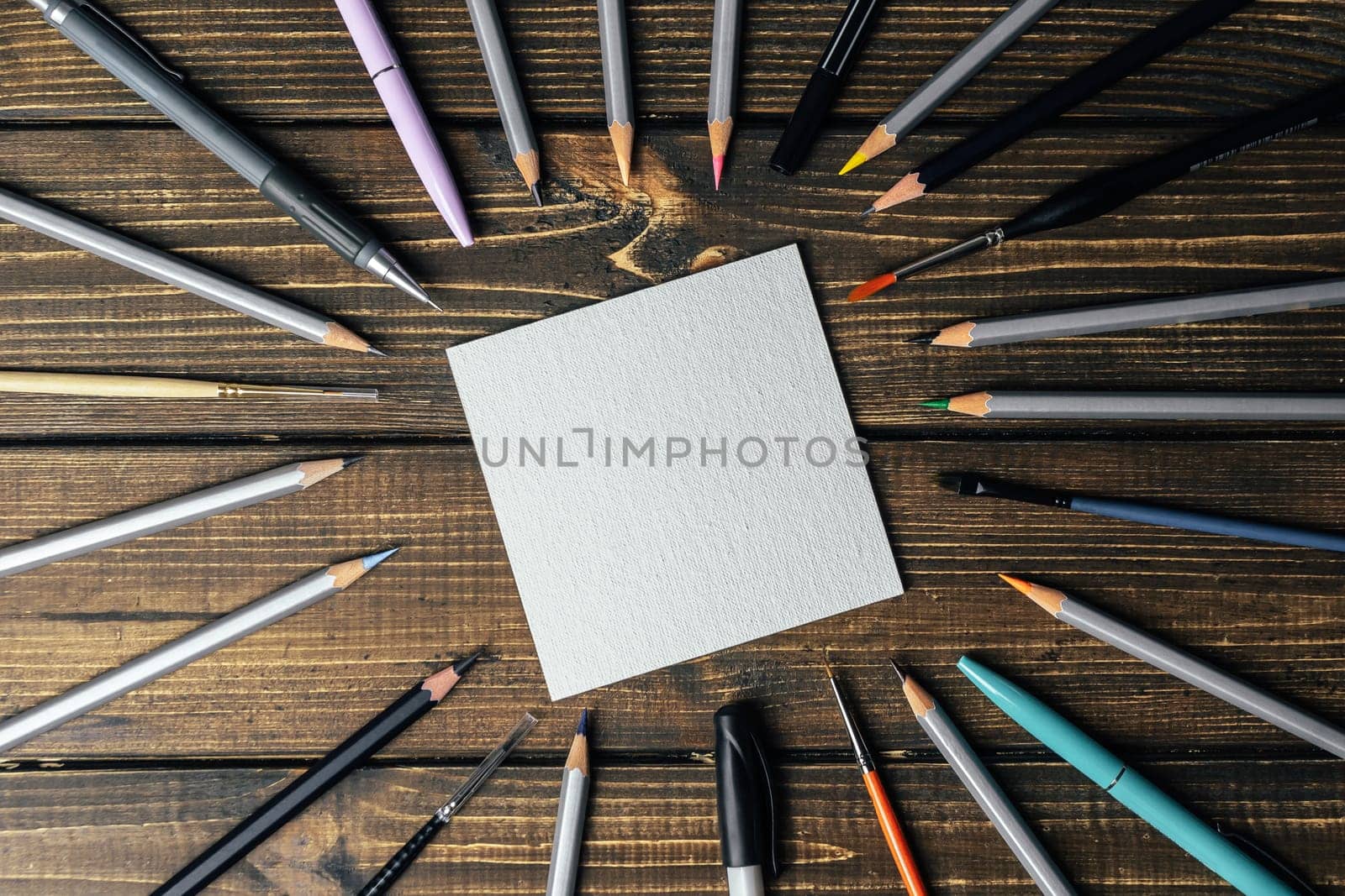 A collection of pens and pencils are arranged in a circle around a blank piece of paper. Concept of creativity and inspiration