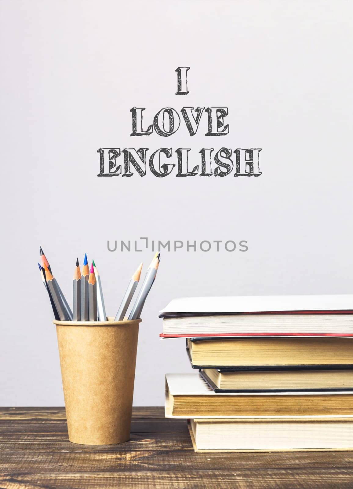 A stack of books and a pencil holder with the words I love English written on the wall behind them