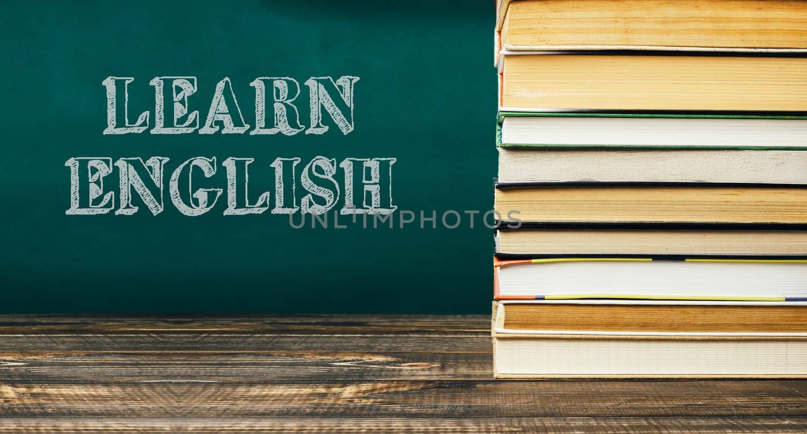 A stack of books with the word learn English written on a green chalkboard. The books are piled on top of each other, creating a sense of importance and emphasis on the subject