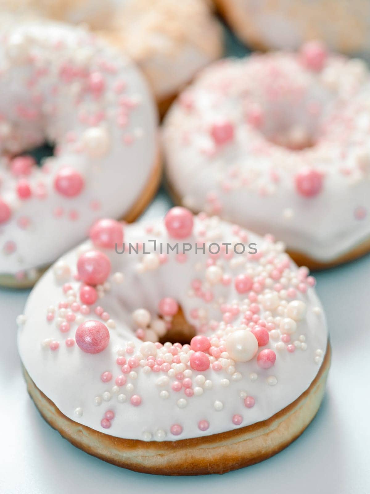 Delicious tender donuts glazed white glaze and sprinkled with pink pearl dressing. Idea decorating donuts for wedding, romantic event, celebration. Selective focus with copy space. Vertical