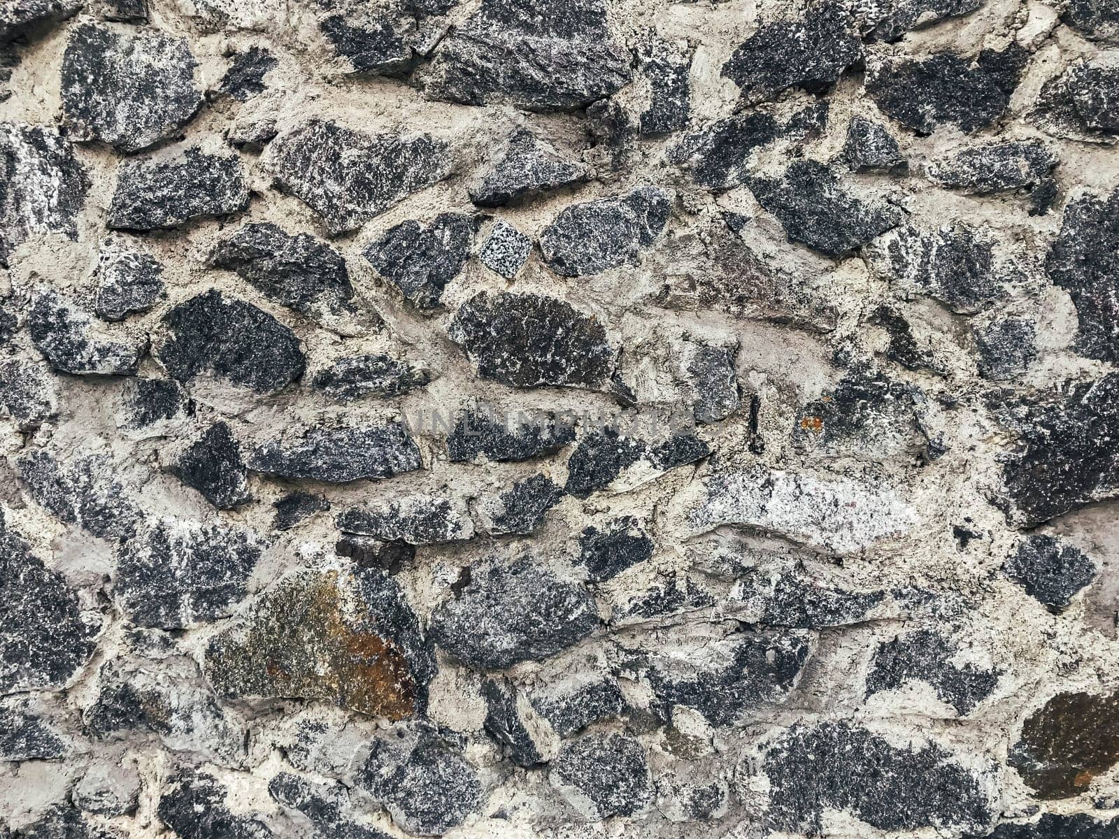 A wall made of stone with a lot of black and white stones. The wall is rough and has a lot of texture