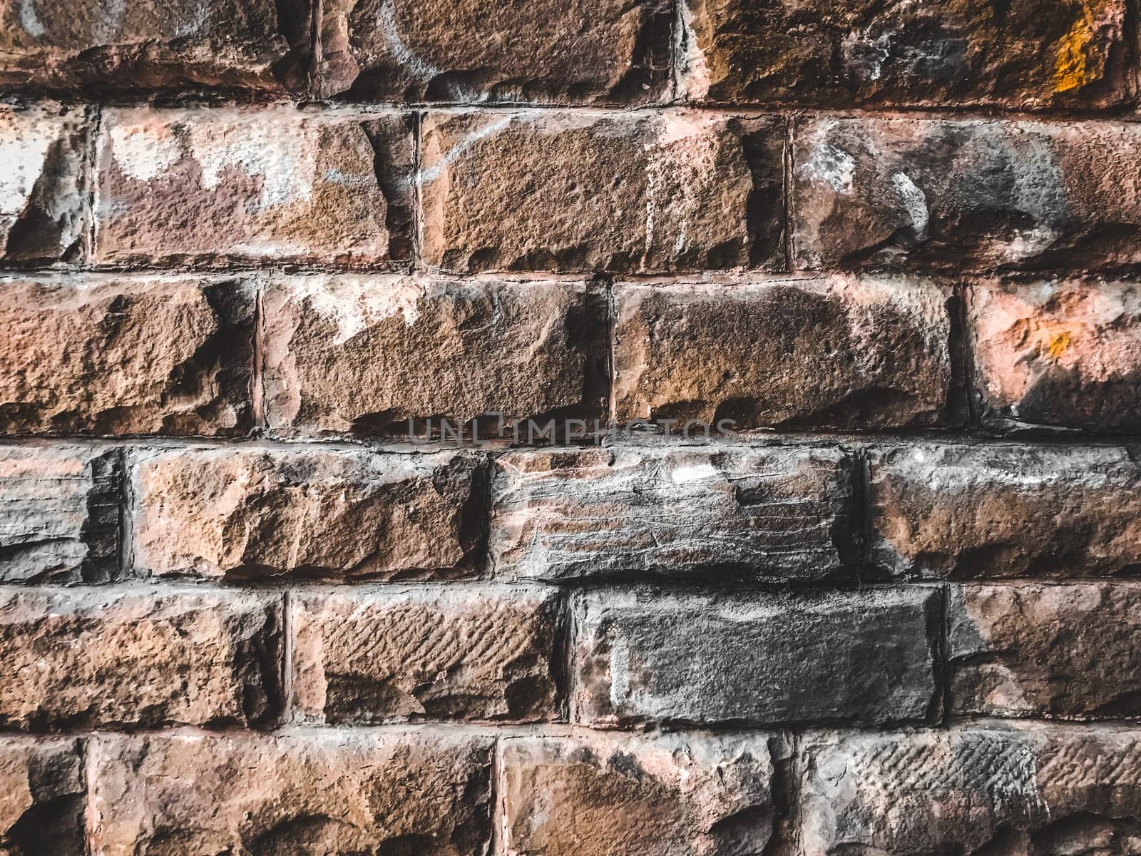 A brick wall with a few white marks on it. The wall is brown and has a rough texture