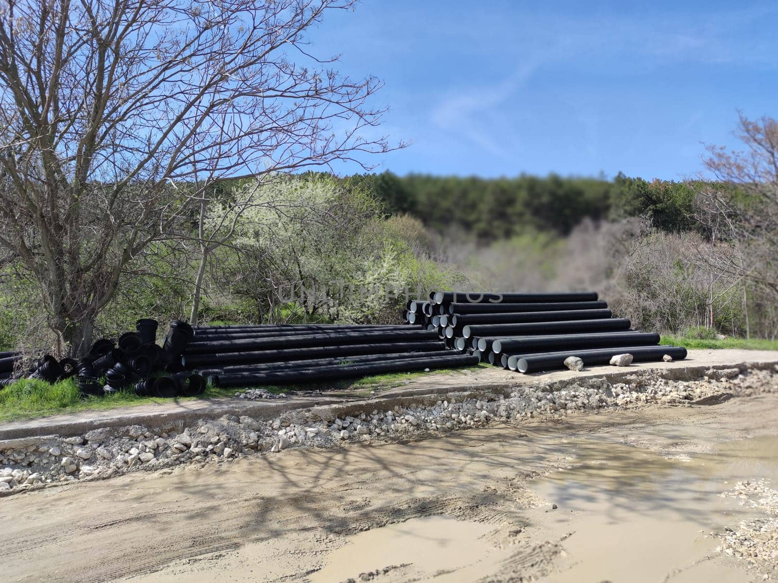 stacked black polyethylene pipes on the side of a road being repaired by Annado