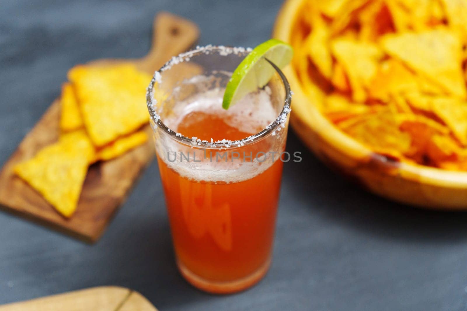 Michelada cocktail with tomato juice, beer and lime in a glass and nachos. Selective focus