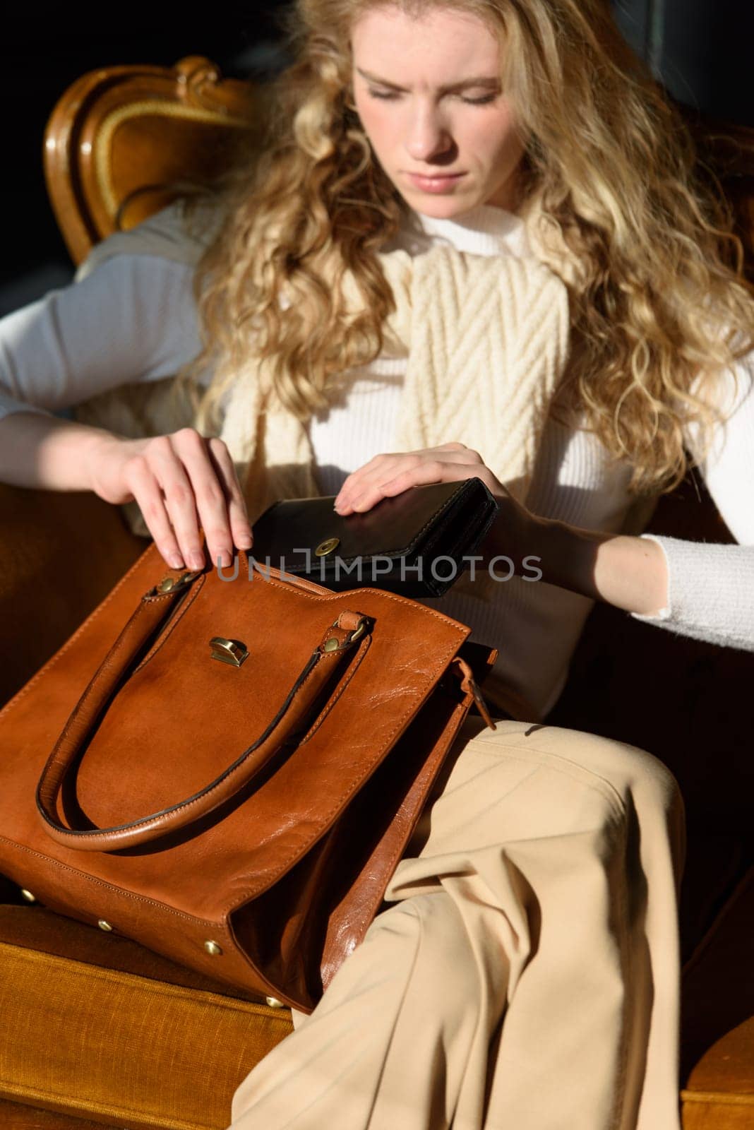 beautiful curly blond hair woman posing with a wallet and small shopper brown bag in a vintage chair by Ashtray25