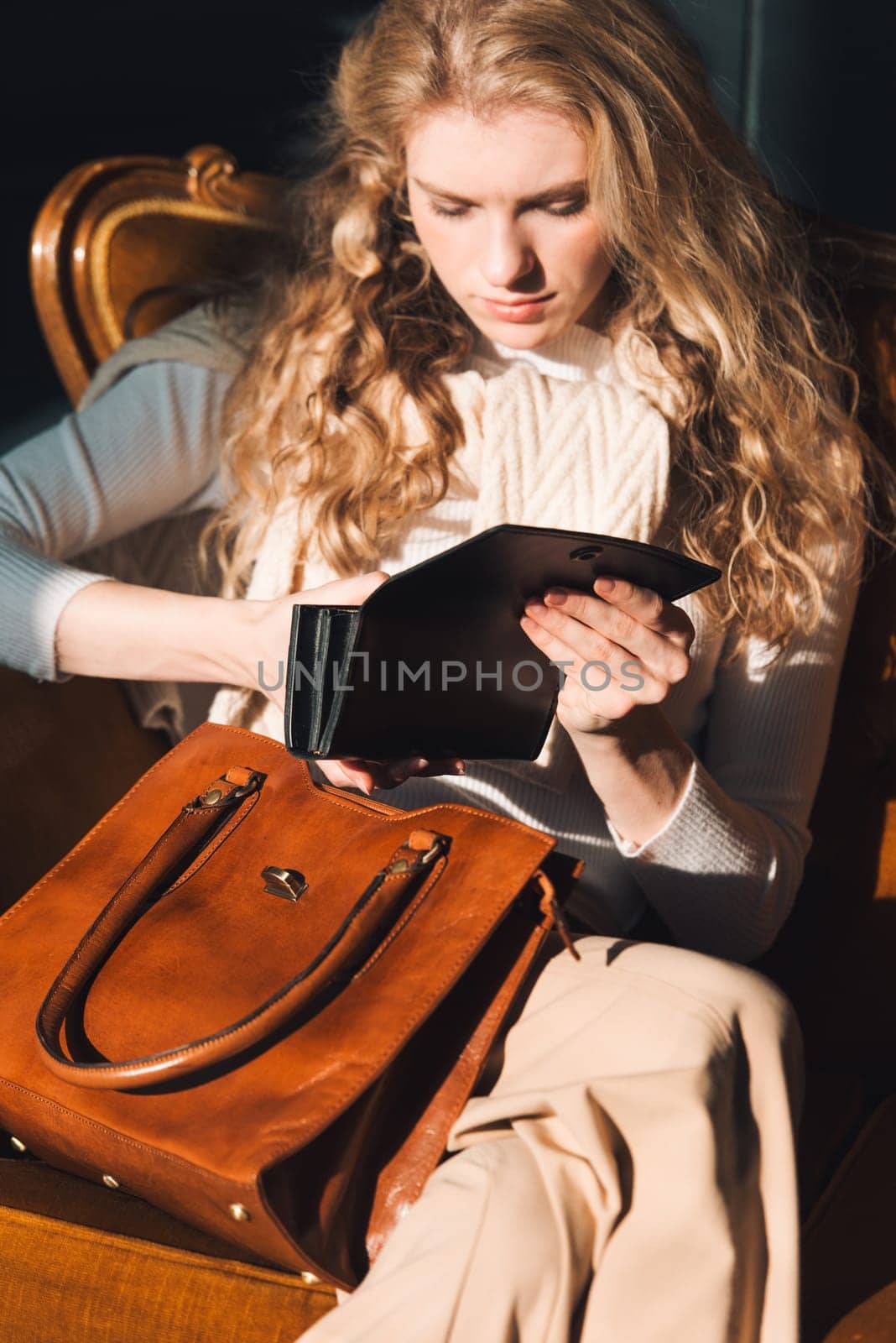 beautiful curly blond hair woman posing with a wallet and small shopper brown bag in a vintage chair by Ashtray25