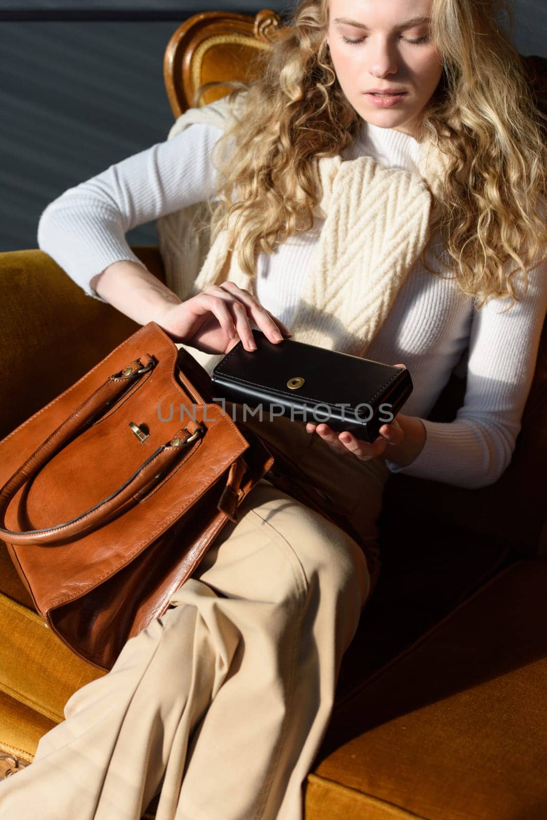 beautiful curly blond hair woman posing with a wallet and small shopper brown bag in a vintage chair by Ashtray25