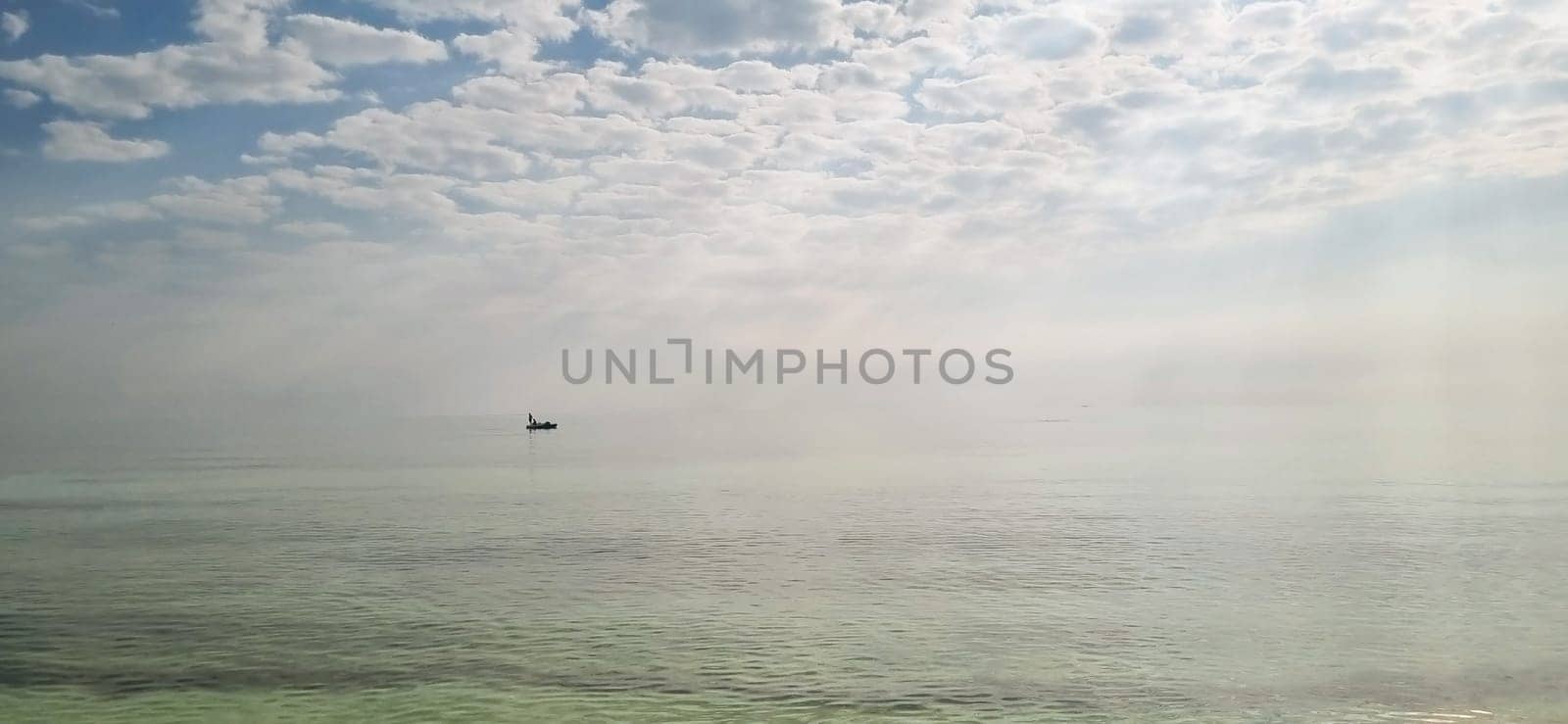 Shot of a man on a small catamaran boat by the horizon, which is hard to detect because of the fog and humidity.