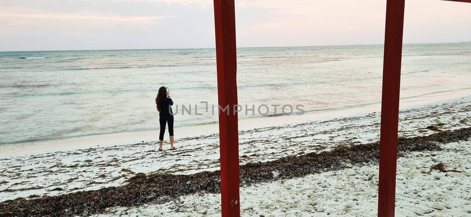 Shot of the woman by the sea shore with the cell phone, at sunrise hour