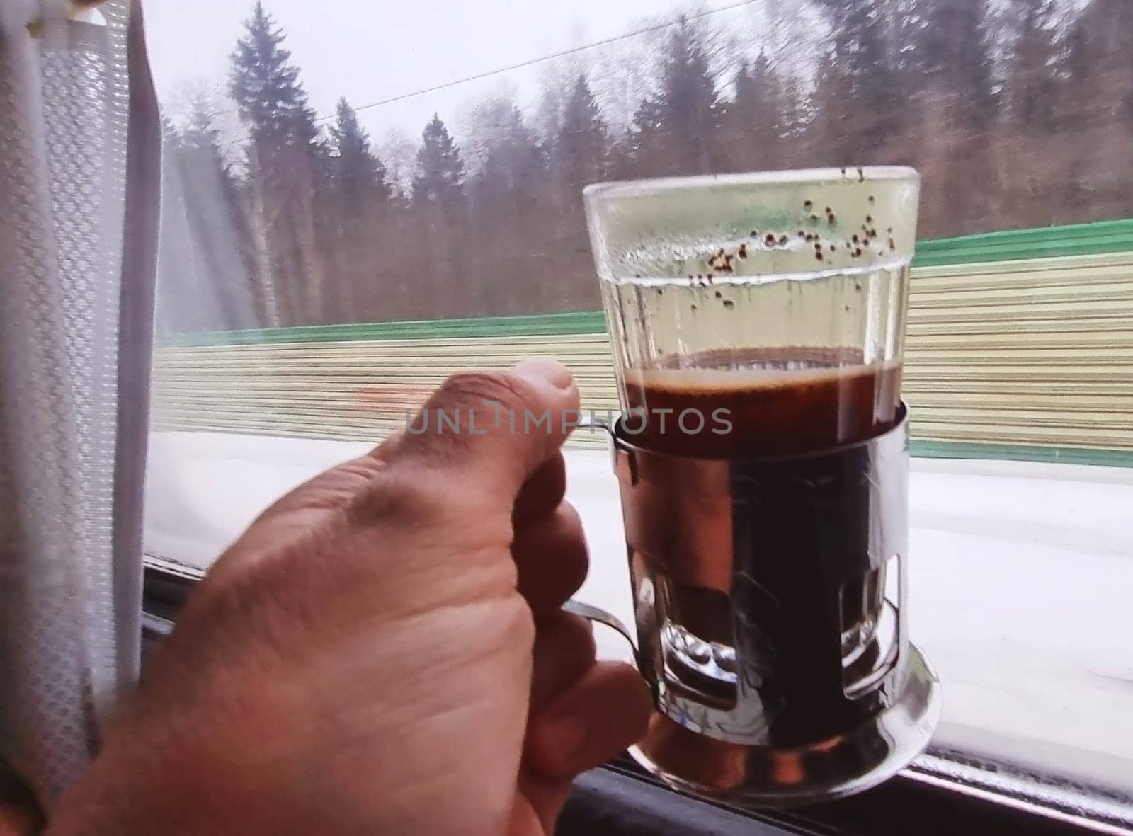Man holds a glass with coffee in the front of train window