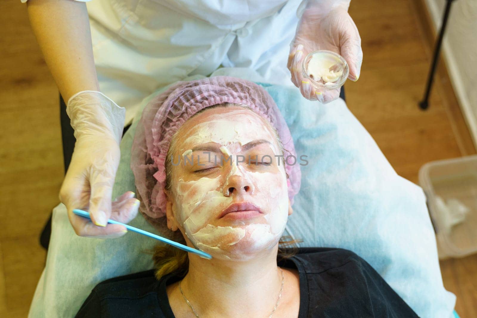 A woman is having a facial mask applied to her face at a spa or beauty salon.