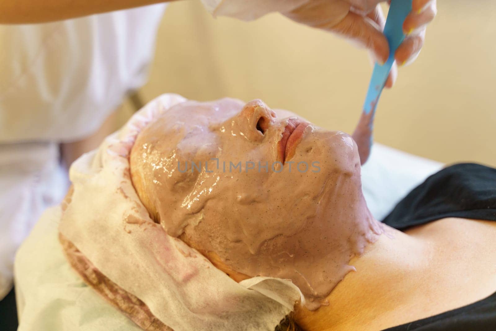 A woman is having a facial mask applied to her face in a beauty salon.