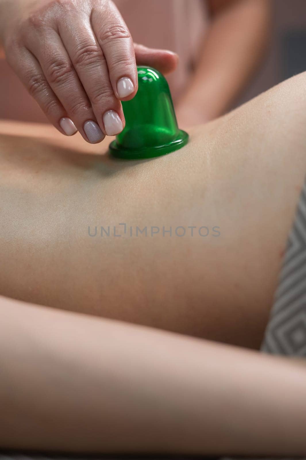 A woman undergoes an anti-cellulite massage procedure using a vacuum jar. Close-up of the lower back. Vertical photo