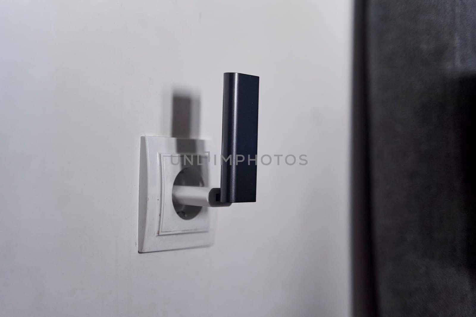 A black wi-fi router is plugged into a white electrical outlet on a grey wall in an art room, near a wooden door with a silver door handle