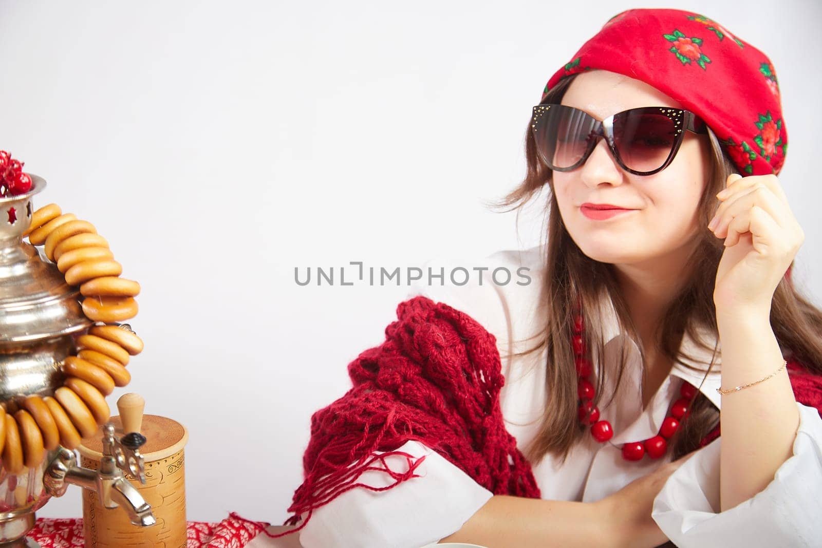 A fashionable modern girl in stylized folk clothes at a table with a samovar, bagels and tea for the Orthodox holiday of Maslenitsa and Easter. Funny photo shoot for a young woman by keleny