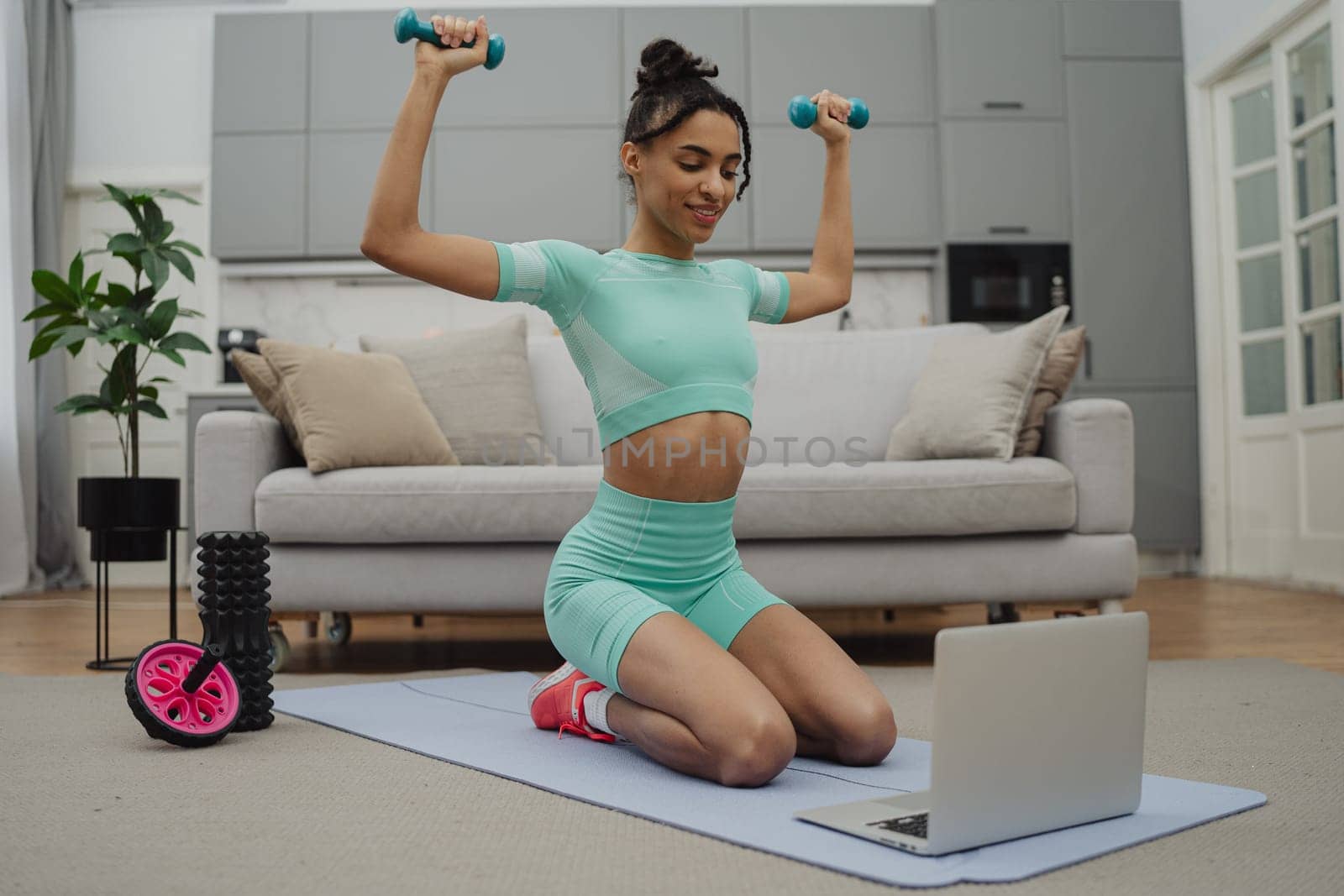 Beautiful young woman in sports clothing exercising at home by Сookiestock