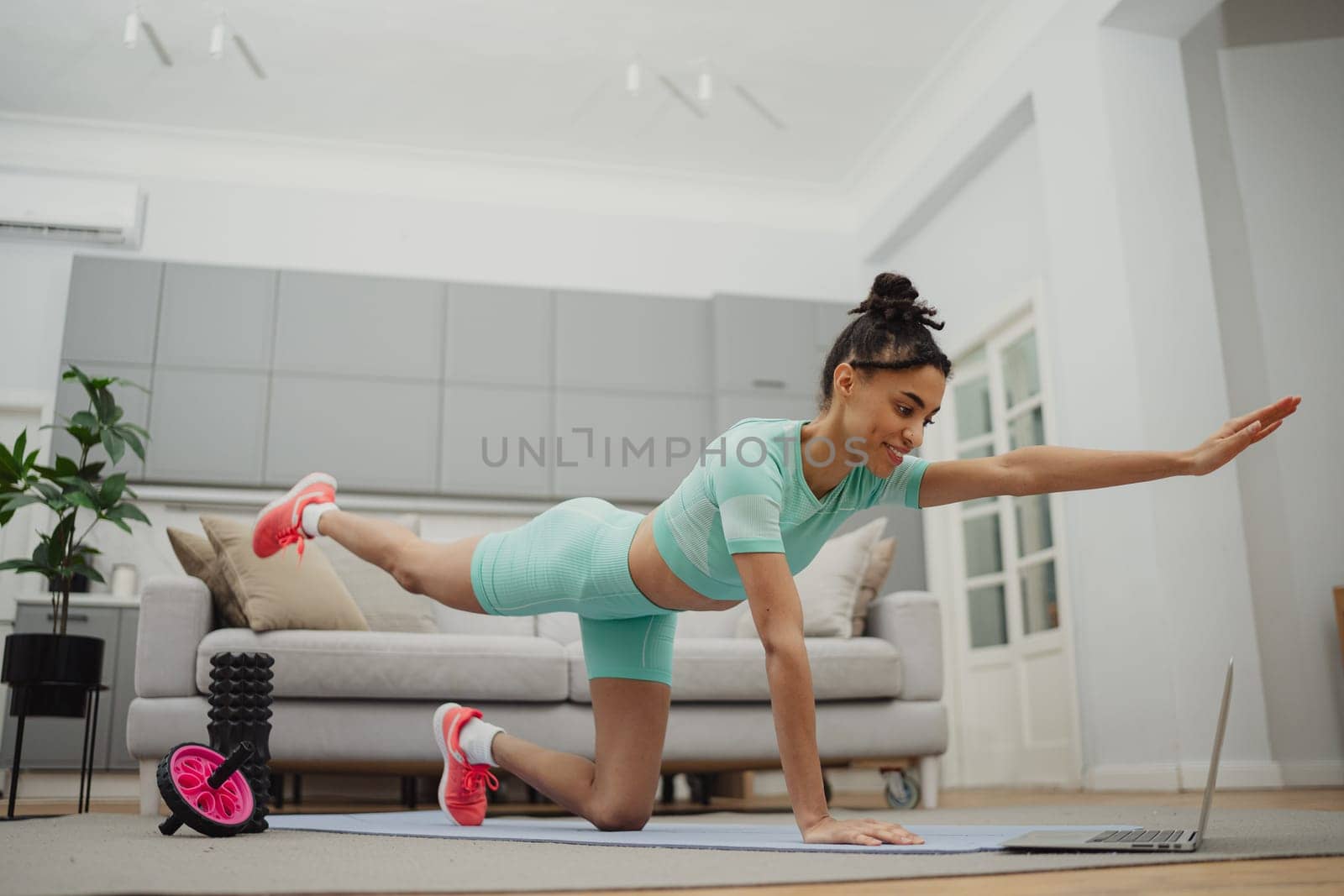 Beautiful young woman in sports clothing exercising at home by Сookiestock