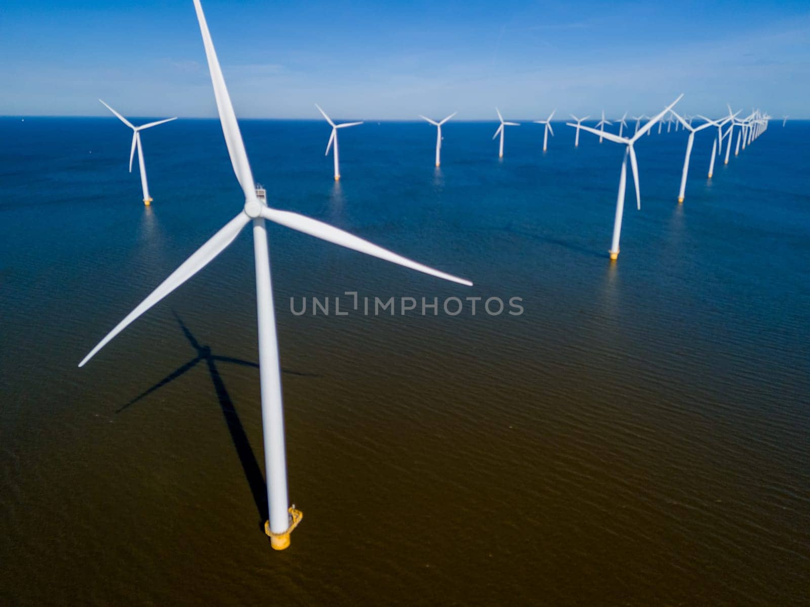 A group of majestic wind turbines standing tall in the ocean against a cloudy sky, harnessing the power of the wind to generate sustainable energy. drone aerial view of windmill turbines