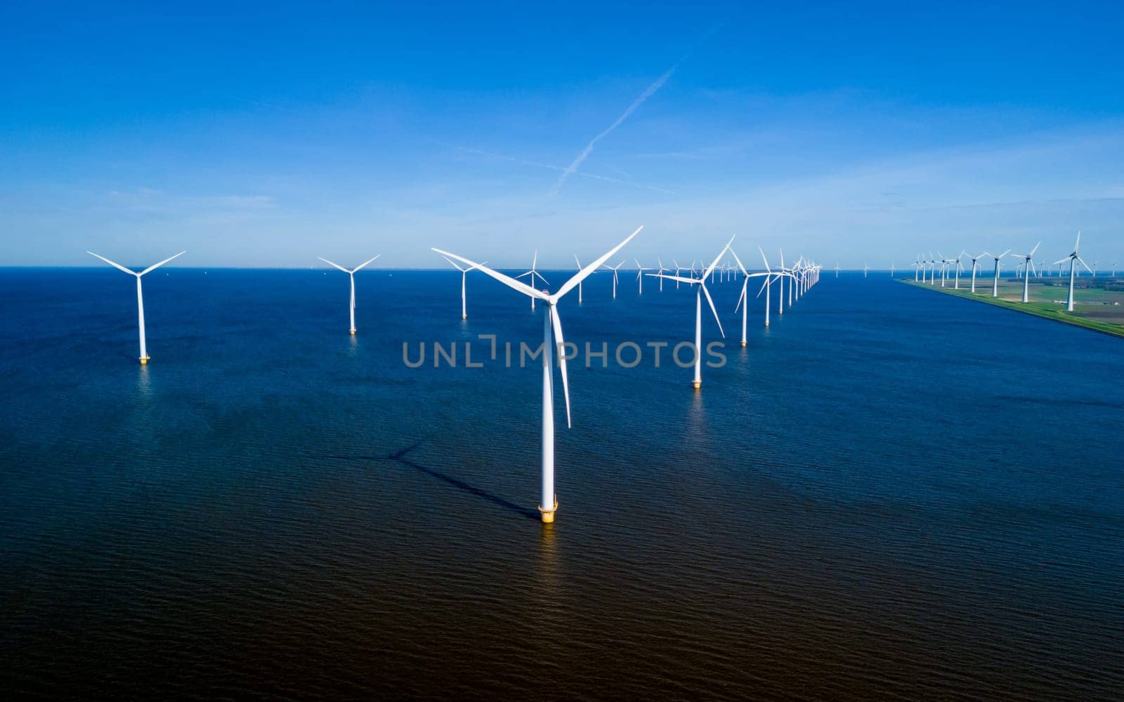 A mesmerizing aerial view of a row of wind turbines swaying gracefully in the ocean breeze off the coast of Flevoland in the Netherlands. windmill turbines energy transition