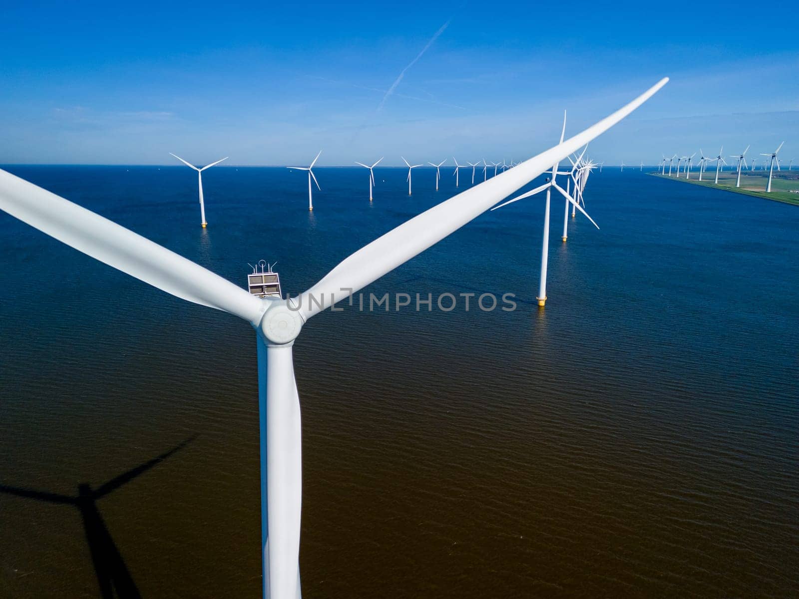 A wind farm with towering turbines stands gracefully in the middle of a vast body of water by fokkebok