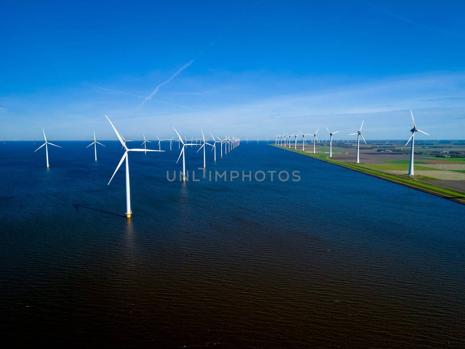 Windmills stand tall in a large body of water, their blades spinning gracefully in the wind, creating a mesmerizing scene of green energy generation in the Netherlands Flevoland in Spring.