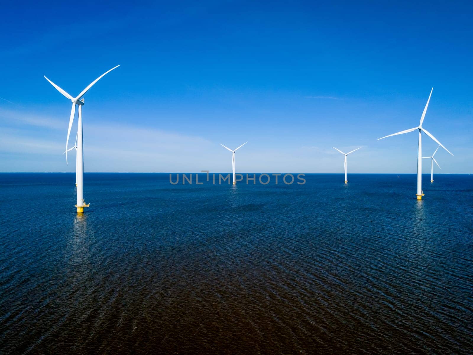 A group of wind turbines gracefully spin above the surface of the ocean in the Netherlands Flevoland during the vibrant season of Spring. drone aerial view of windmill turbines green energy