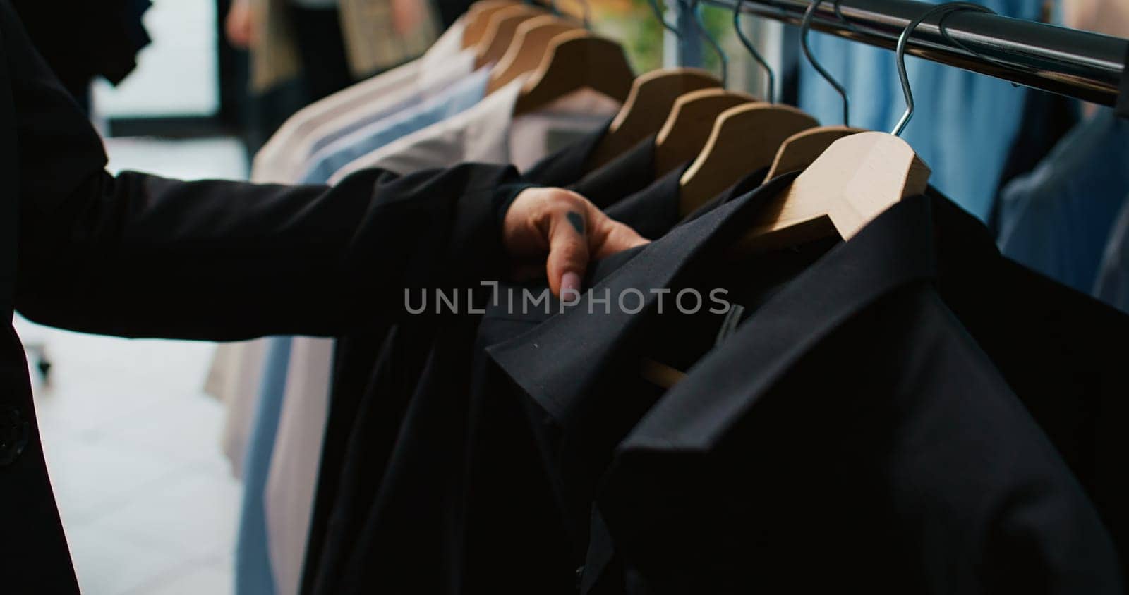 Classy woman examining all colorful shirts on display at clothing store, shopping for trendy brands to expand wardrobe. Customer looking at fashion items stored on hangers. Close up. Camera B.