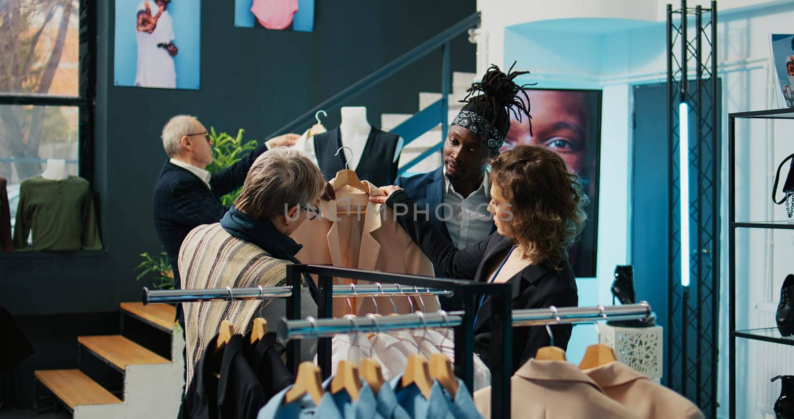 Employees team presenting variety of clothes to senior client, helping her to choose the perfect shirt size to create a formal outfit. Diverse store assistants show clothing from designers. Camera B.