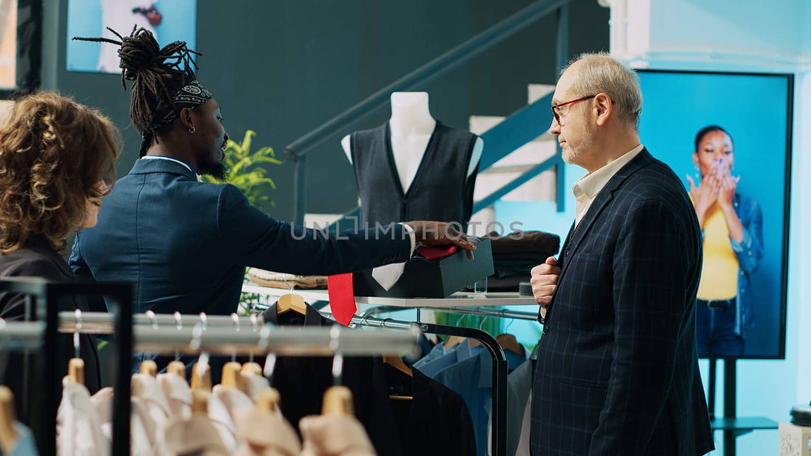 Fashion stylist making trendy recommendations for senior client, pairing an expensive tie to match a black elegant shirt. African american worker selling designer items to man. Camera A.