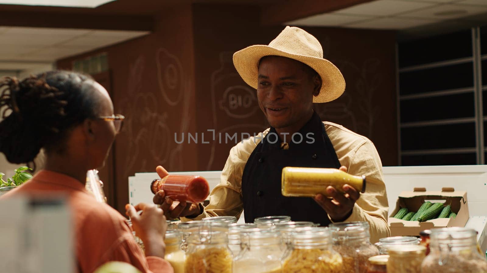 Merchant presenting additives free homemade sauces for tasty meals, recommending ethically sourced pantry supplies and pasta. Seller promoting his organic bulk products in glass jars. Camera 1.