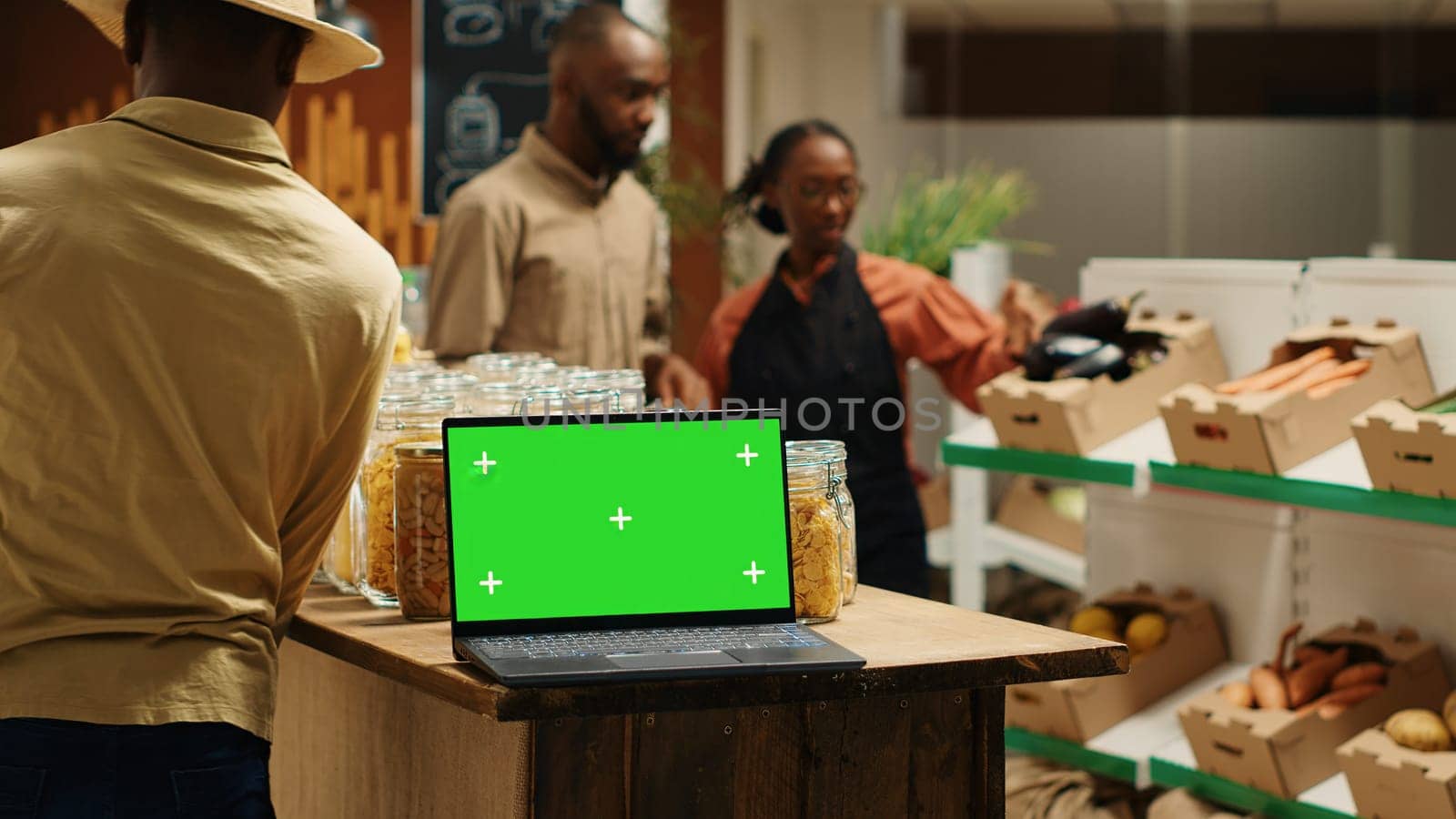 Laptop on stall at supermarket showing greenscreen template, people shopping for organic homegrown products in zero waste eco store. Portable pc with blank chromakey and copyspace. Camera 1.