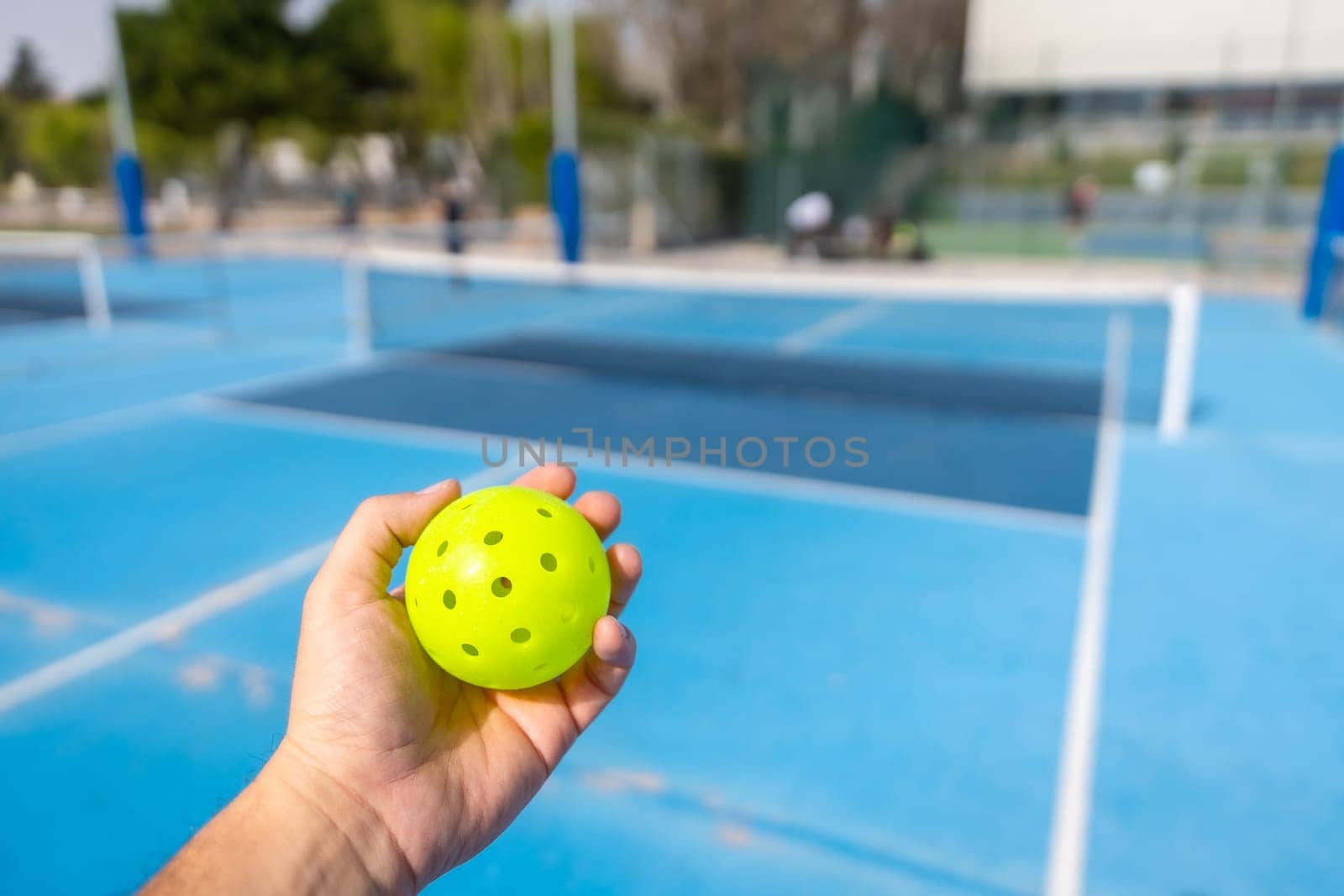 Unrecognizable person holding a plastic yellow pickleball ball by Huizi