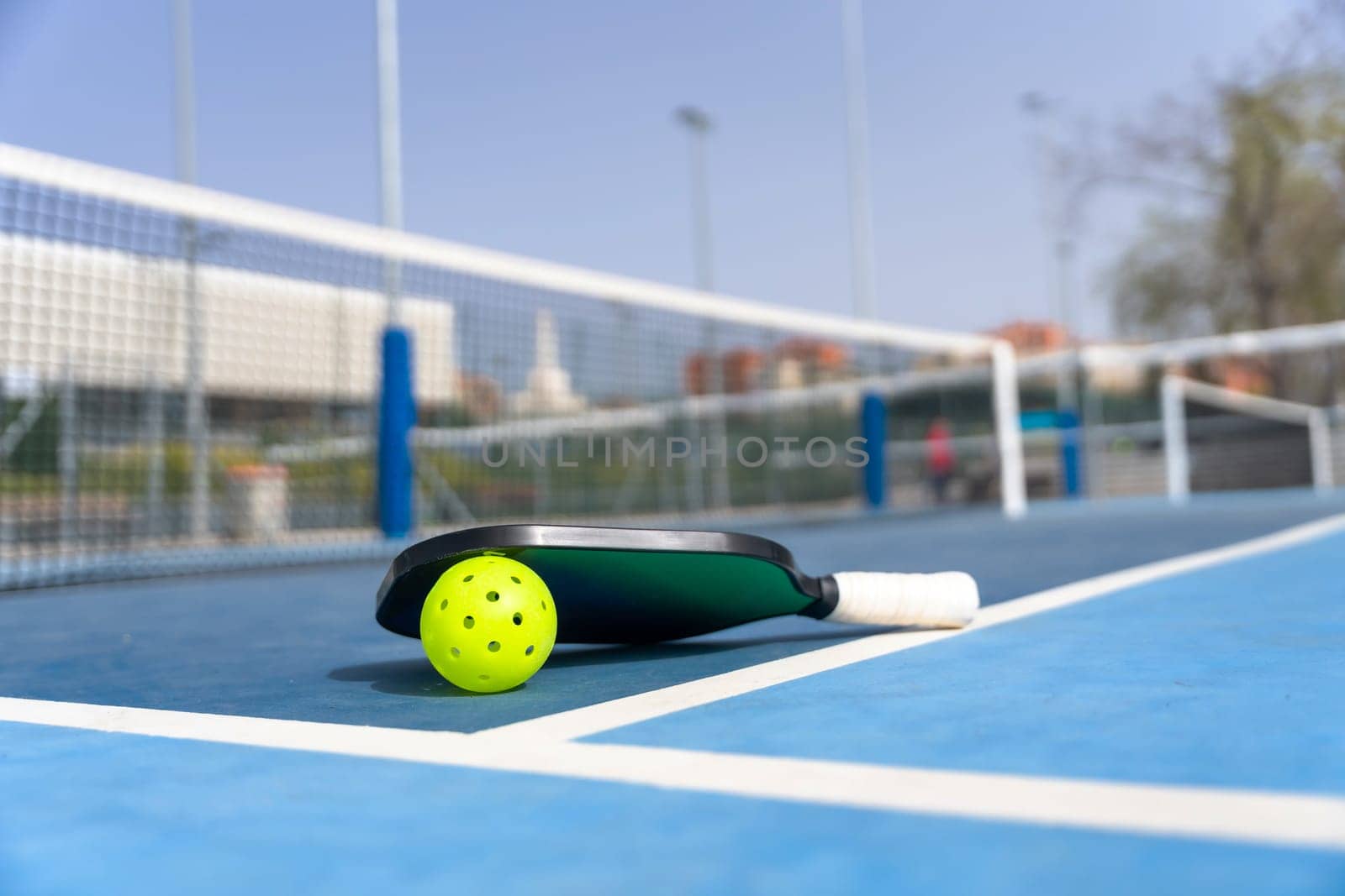 Pickleball ball and racket on the ground of a court by Huizi