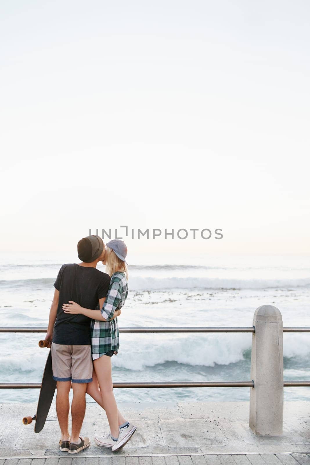 Couple, kiss and romance on beach for date with mockup space, adventure and skateboard on promenade. Skater, people and hugging on boardwalk for bonding, embrace and outdoor travel with sea waves.