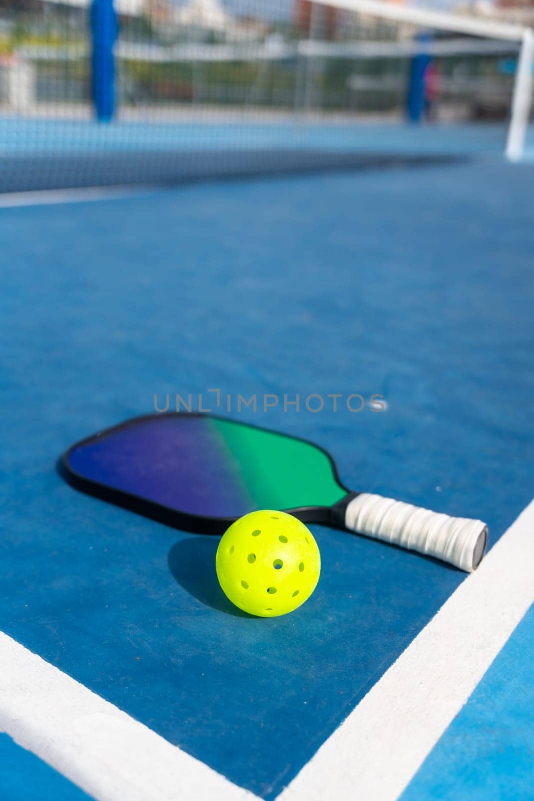Vertical photo of a racket and pickleball ball placed on the ground on a blue court