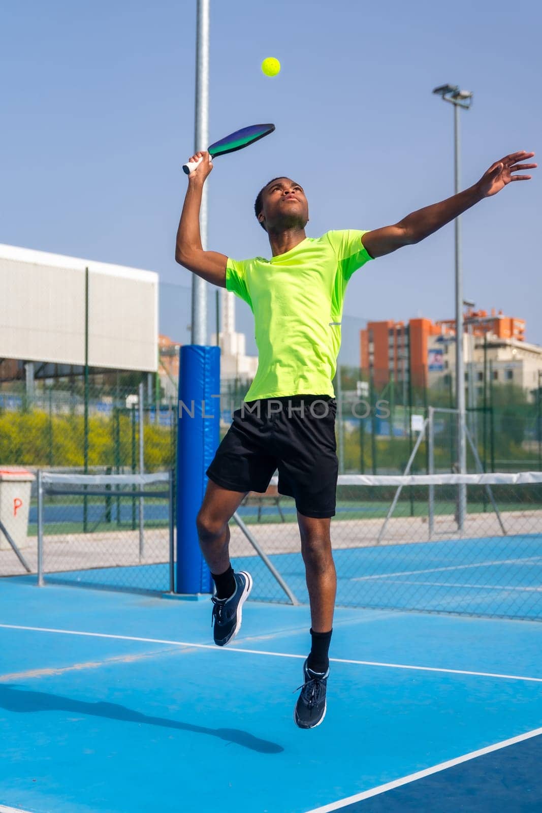 African man jumping to hit the ball playing pickleball outdoors by Huizi