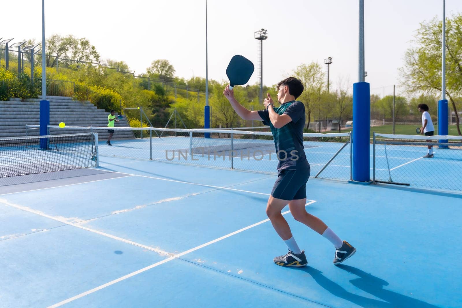 Full length rear view of a sportive young man playing pickleball in an outdoor blue court